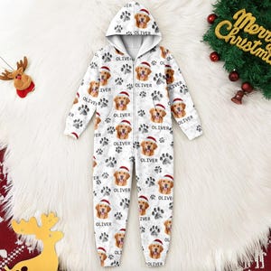 May include: White hooded onesie with a repeating pattern of a Golden Retriever wearing a Santa hat, paw prints, and the name "OLIVER". The onesie has a zipper closure and is designed for Christmas.