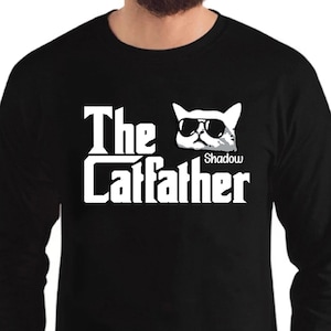 May include: Black long-sleeve t-shirt with a white graphic of a cat wearing sunglasses and the text "The Catfather" with the name "Shadow" below the cat.