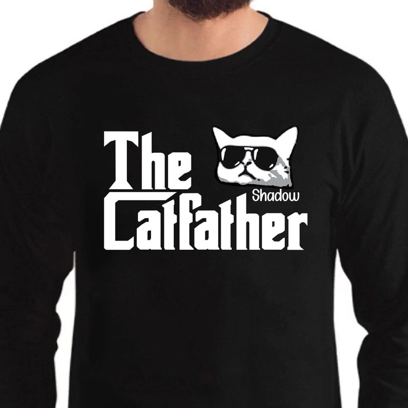 May include: Black long-sleeve t-shirt with a white graphic of a cat wearing sunglasses and the text "The Catfather" with the name "Shadow" below the cat.