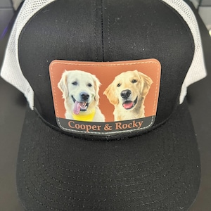 May include: Black and white mesh trucker hat with a brown patch featuring two golden retriever dogs with the text "Cooper & Rocky" on the patch.