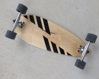 Könnte beinhalten: Ein Longboard aus Holz mit schwarzen diagonalen Streifen. Das Board hat schwarze Räder und silberne Achsen.
