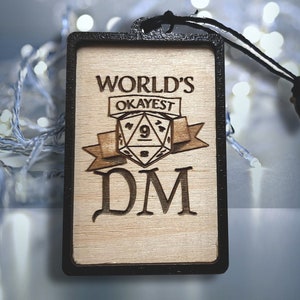 May include: A wooden ornament with a black border, featuring the text "WORLD'S OKAYEST DM" and a stylized image of a nine-sided die.