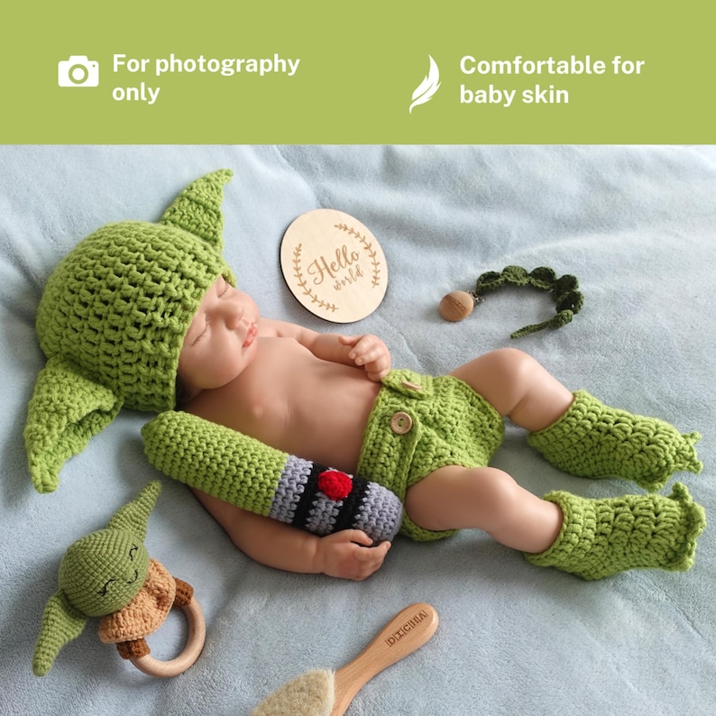 Op de afbeelding: Een pasgeboren baby in een groen gehaakt Yoda-thema-outfit, inclusief een hoed, shorts en beenwarmers. Accessoires zijn onder meer een lichtzwaard, een houten bord met "Hello world" en een rammelaar. De tekst in de afbeelding zegt "For photography only" en "Comfortable for baby skin".