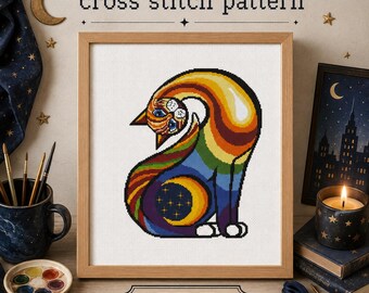 May include: A cross stitch pattern PDF featuring a stylized cat with a rainbow-colored body, a crescent moon and stars on its flank, and blue eyes. The design is displayed in a wooden frame with the text cross stitch pattern and PDF visible.
