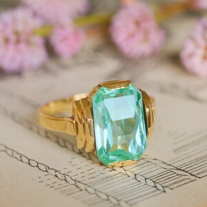 May include: A gold ring with a large, light blue, emerald-cut gemstone.