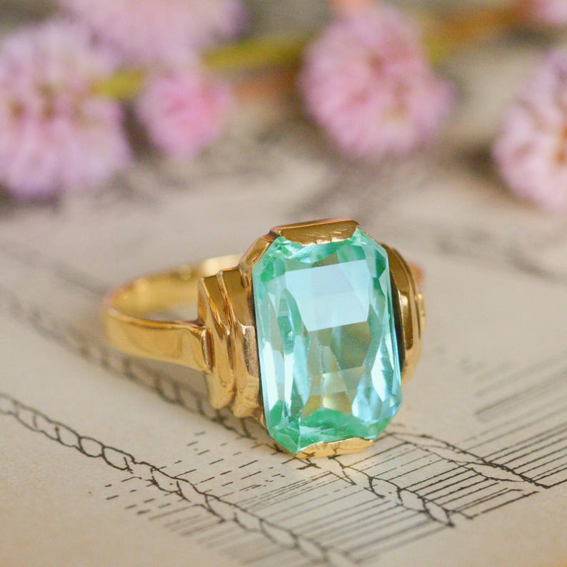 May include: A gold ring with a large, light blue, emerald-cut gemstone.