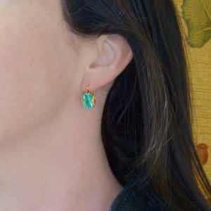 May include: Gold earrings with a single emerald green gemstone.
