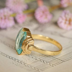 May include: A gold ring with a large, faceted, light blue gemstone. The ring has a simple, elegant design.