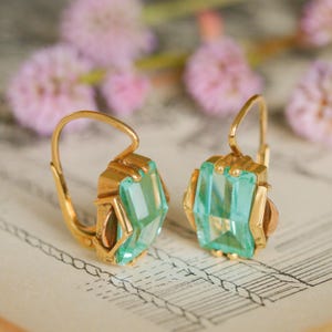 May include: A pair of gold earrings with light green gemstone accents. The earrings have a simple, elegant design and are perfect for everyday wear.