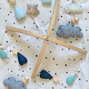 May include: A wooden baby mobile with felt clouds, stars, and raindrops hanging from it. The mobile is suspended from a wooden frame and has a white background with black polka dots.