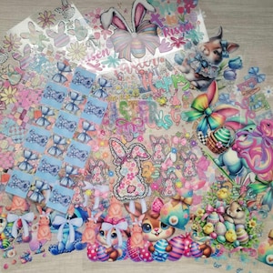 May include: A collection of Easter-themed stickers featuring bunnies, eggs, bows, and flowers. The stickers are on clear sheets and are perfect for adding a festive touch to crafts, cards, and gifts.