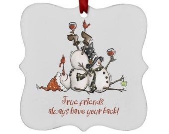 May include: A white metal ornament with a whimsical illustration of three snowmen holding glasses of wine. The snowmen are wearing hats and scarves. The ornament has the text "True friends always have your back!"