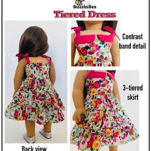 May include: A doll wearing a tiered dress with a floral print and a contrasting pink band detail. The dress has a 3-tiered skirt and a back view of the doll is also shown. The dress is called "Tiered Dress" and the brand is "BuzzinBea".