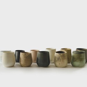 Peut inclure: Ensemble de verres à vin sans pied en céramique, aux couleurs variées : crème, noir et vert olive. Les verres ont une forme arrondie et une surface texturée, parfaits pour servir des boissons.