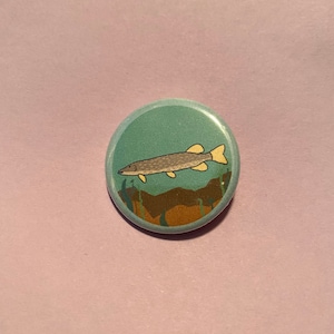 May include: A round button with a green background featuring a cartoon illustration of a fish swimming in water with brown and green plants.