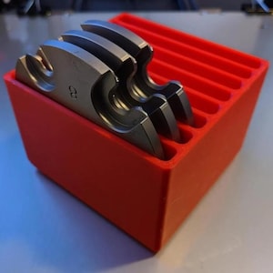 Puede incluir: Una caja de almacenamiento de plástico roja con seis compartimentos, que contiene un juego de cinco anillos de metal plateado con el número "2" impreso en uno de los anillos.