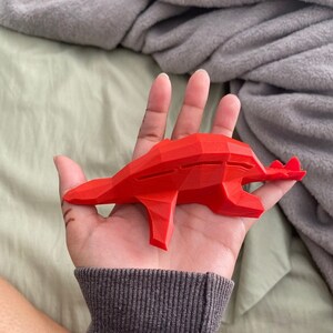 May include: A red 3D printed dragon figurine with a geometric design. The dragon is posed in a flying position with its wings spread out.