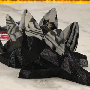 May include: A black 3D printed guitar pick holder with five guitar picks. The picks are white and black with a swirl pattern and have the word "JIMMY" written on them.