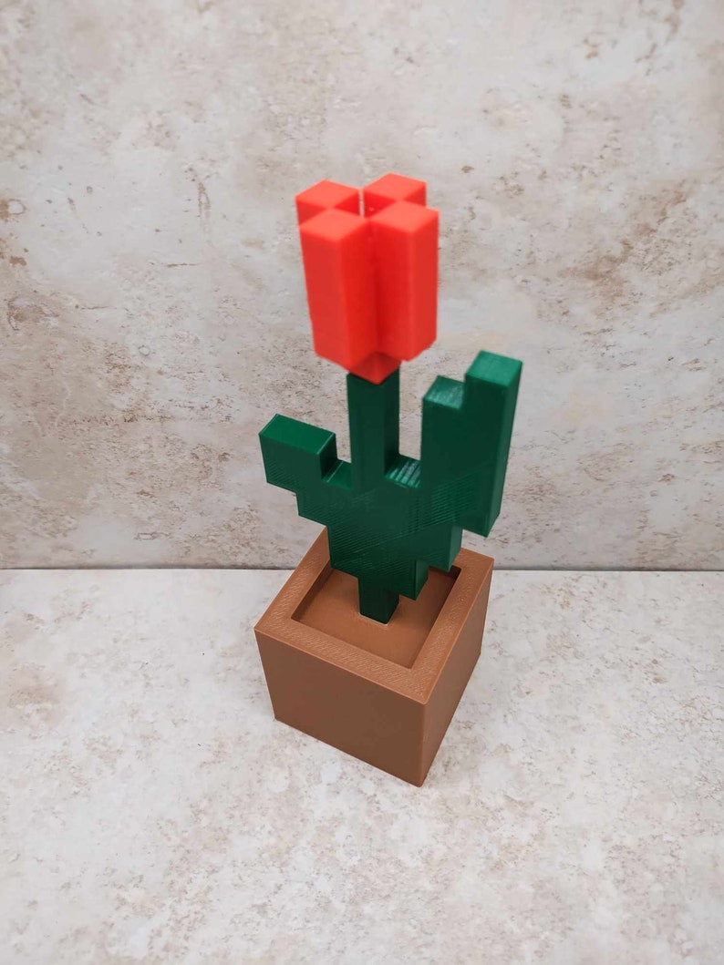 May include: A 3D printed Minecraft-style red flower in a brown pot with a green stem and leaves.
