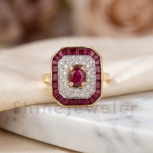 May include: A gold ring with a rectangular face. The face features a central oval ruby surrounded by a halo of small diamonds. A border of square-cut rubies frames the diamonds, creating a striking contrast.
