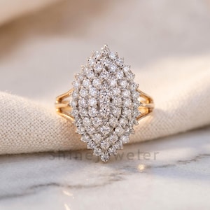 May include: A marquise-shaped cluster ring featuring numerous small, round, brilliant-cut white diamonds set in a yellow gold band. The central arrangement consists of multiple tiers of stones creating a dense, sparkling, elongated floral-like pattern.