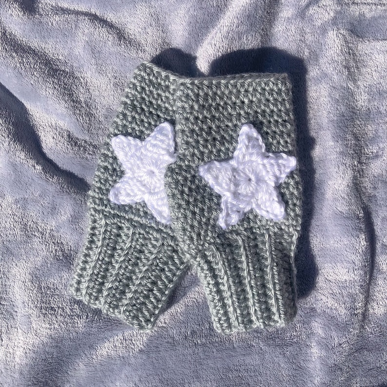 light grey crocheted fingerless gloves with ribbing detail around wrist and white star motif on back of hand