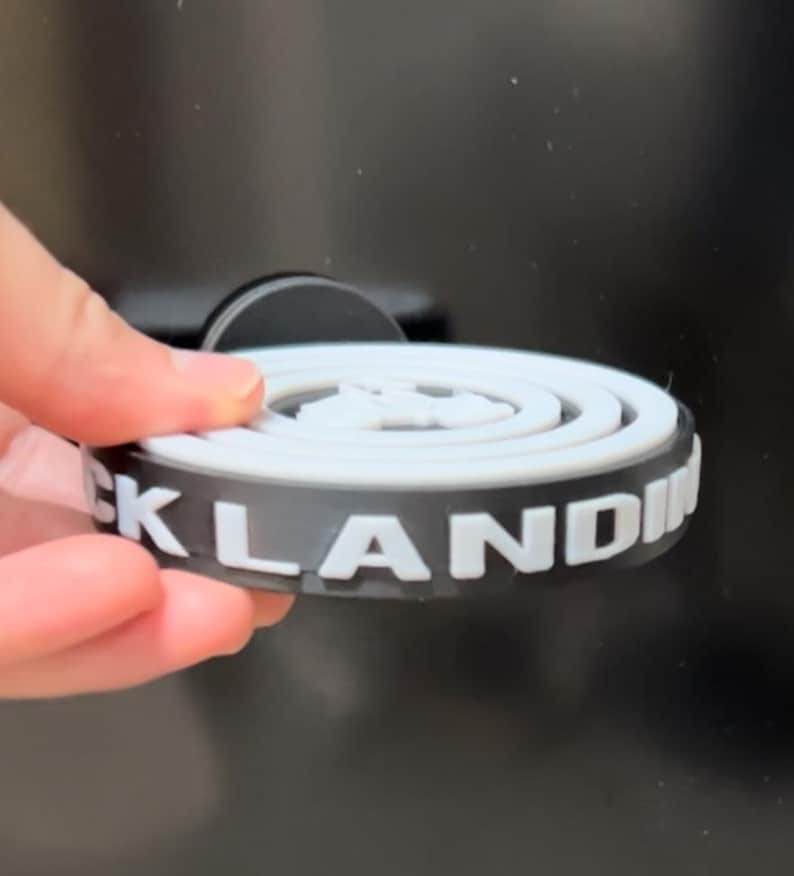 May include: A black and white circular object with the word "CKLANDIN" printed on the side. The object is held by a hand against a dark background. The object has a white interior design.