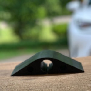 May include: A black plastic cable management ramp with a rounded top and a hole in the center. The ramp is designed to help keep cables organized and prevent them from being damaged.