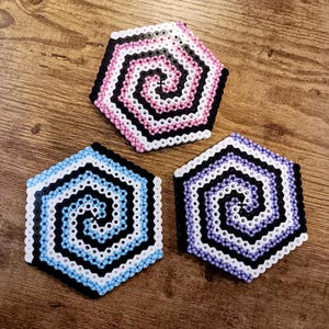 May include: Three hexagonal coasters with a spiral pattern in black, white, pink, and purple.