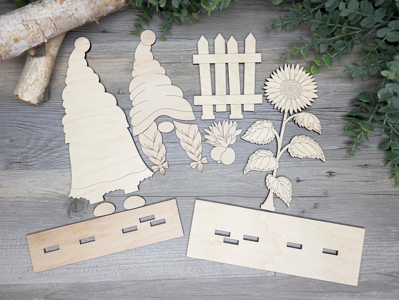 May include: Wooden craft kit featuring two gnomes, a picket fence, a sunflower, and two wooden bases. The kit is designed for painting and decorating.