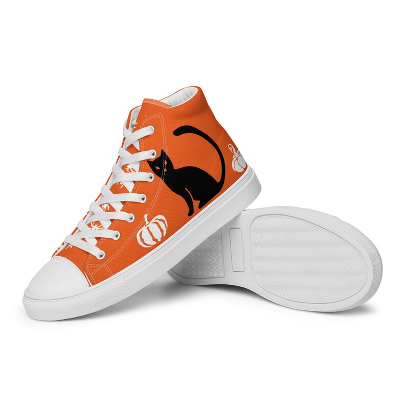 Puede incluir: Zapatillas altas naranjas con cordones y suelas blancas. Las zapatillas presentan una silueta de gato negro y gr&aacute;ficos de calabazas blancas. Los zapatos est&aacute;n dise&ntilde;ados con un tema de Halloween.