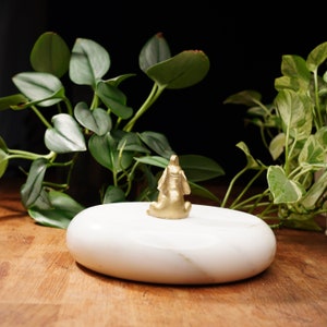 May include: A small gold elephant figurine sitting on a white marble oval-shaped base.