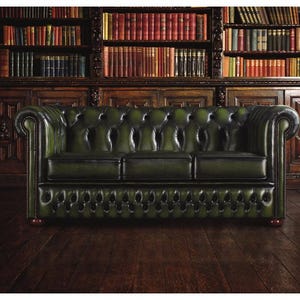 Può includere: Un divano Chesterfield in pelle verde con trapuntatura, posto di fronte a una libreria in legno piena di libri. Il divano ha braccioli arrotolati e un design classico, ideale per una biblioteca o un soggiorno.