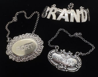 Può includere: Tre etichette per bottiglie in argento con catene. Le etichette sono incise con le parole "BRANDY", "PORT" e "SHERRY".