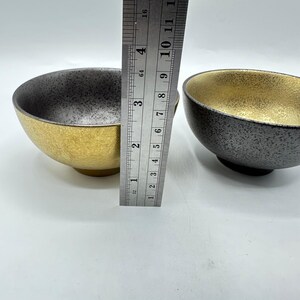 May include: Two small ceramic bowls with a speckled exterior and a metallic gold interior. The bowls are approximately 3 inches in diameter. One bowl has a gold exterior, and the other has a dark gray exterior.