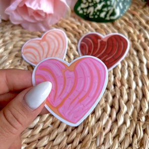 May include: Three heart-shaped stickers with a swirl pattern. The stickers are pink, red, and white.