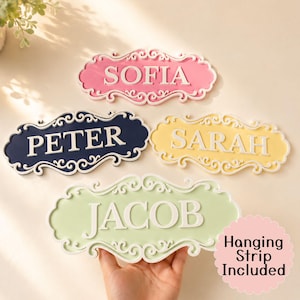 May include: Four decorative name plaques with ornate, swirling borders. The plaques are coloured pink, navy blue, yellow, and light green, each featuring white raised lettering that spells out the names SOFIA, PETER, SARAH, and JACOB respectively.