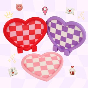 May include: Three heart-shaped stands with a checkered pattern. One stand is red with a red and white checkerboard center, one is purple with a purple and white center, and one is light pink with a pink and white checkerboard center.