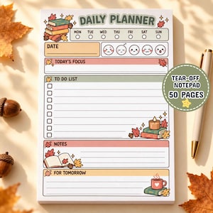 May include: A daily planner notepad featuring an autumn-themed design with illustrations of stacked books, fallen leaves, acorns, a candle, and a mug. The layout includes sections for date, focus, to-do list, notes, and tomorrow, with a mood tracker.