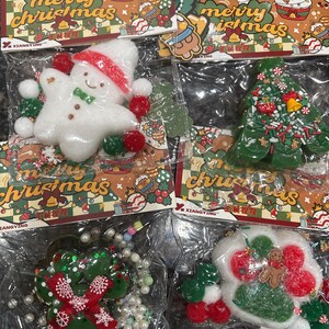 May include: Christmas-themed ornaments in clear plastic packaging. The ornaments include a snowman, Christmas tree, and other festive shapes. The packaging features the text "merry christmas" and decorative illustrations.