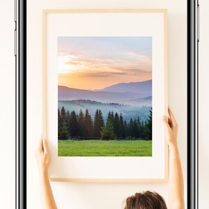 Op de afbeelding: Een smartphone toont een ingelijste landschapsfoto van bergen en bomen onder een kleurrijke lucht. De tekst "MASTER PHOTO LIGHTING ON YOUR PHONE" staat bovenaan. Een persoon houdt het frame vast.