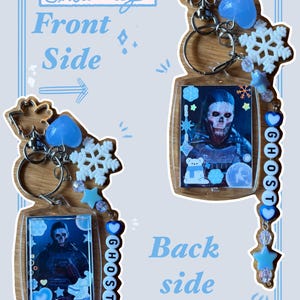 Puede incluir: Dos llaveros con una imagen de personaje, copos de nieve y detalles en azul. Un lado dice "Front Side" y el otro "Back Side". La palabra "GHOST" está escrita con cuentas azules. Los llaveros tienen un tema invernal.