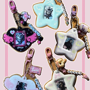 May include: A collection of handmade keychains in star and heart shapes. Each keychain features a small framed image, decorative beads, and a lobster clasp. The keychains are in pastel colors with the word "GHOST" spelled out in beads.