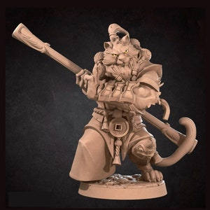 May include: A detailed miniature figurine of a cat-like creature with a staff, wearing a robe and armor. The figurine is painted in a light brown color and has a detailed face with yellow eyes.