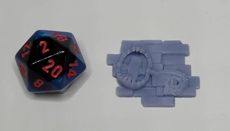 May include: A blue and black 20-sided die with red numbers, and a purple 3D printed miniature of a brick wall with a hole in it.