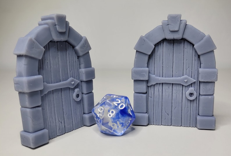 May include: Two gray stone arched doorways with wooden doors, each with a metal handle and a metal hinge. A blue and white 20-sided die sits in front of the doors.