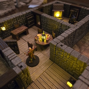 May include: A miniature dungeon scene with stone walls, wooden floors, and a round table set for a meal. A small figure stands in the foreground. The scene is lit with warm, yellow lights, creating a cozy atmosphere.