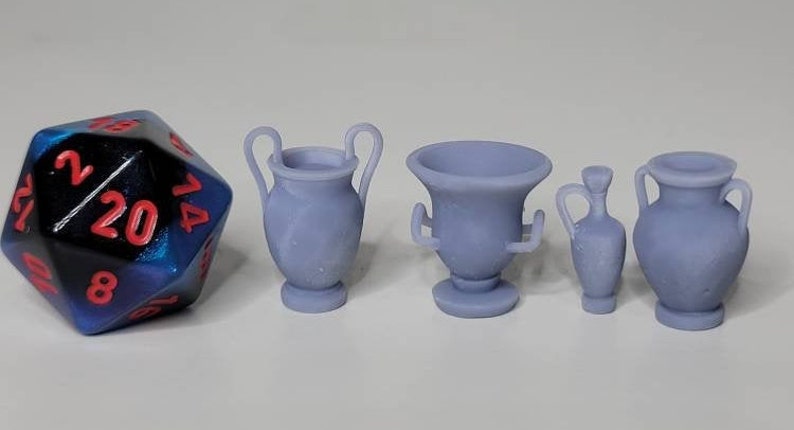 May include: Four miniature ceramic urns in various styles, including a tall urn with two handles, a shorter urn with a wide base, and two smaller urns with a narrow base. The urns are all a light gray color and are arranged on a white surface.