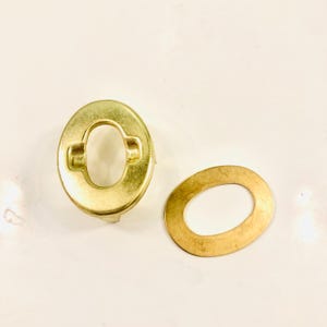May include: Two gold-colored metal snap fasteners. One fastener has a round, oval-shaped hole in the center. The other fastener is a flat, oval-shaped ring.
