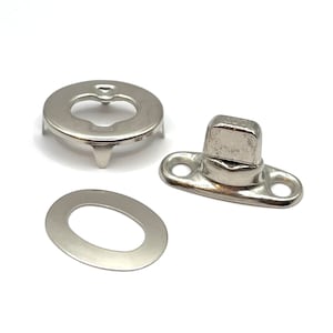May include: A set of three silver metal snap fasteners. The set includes a round base with three prongs, a flat oval piece with a hole in the center, and a stud with a square head.